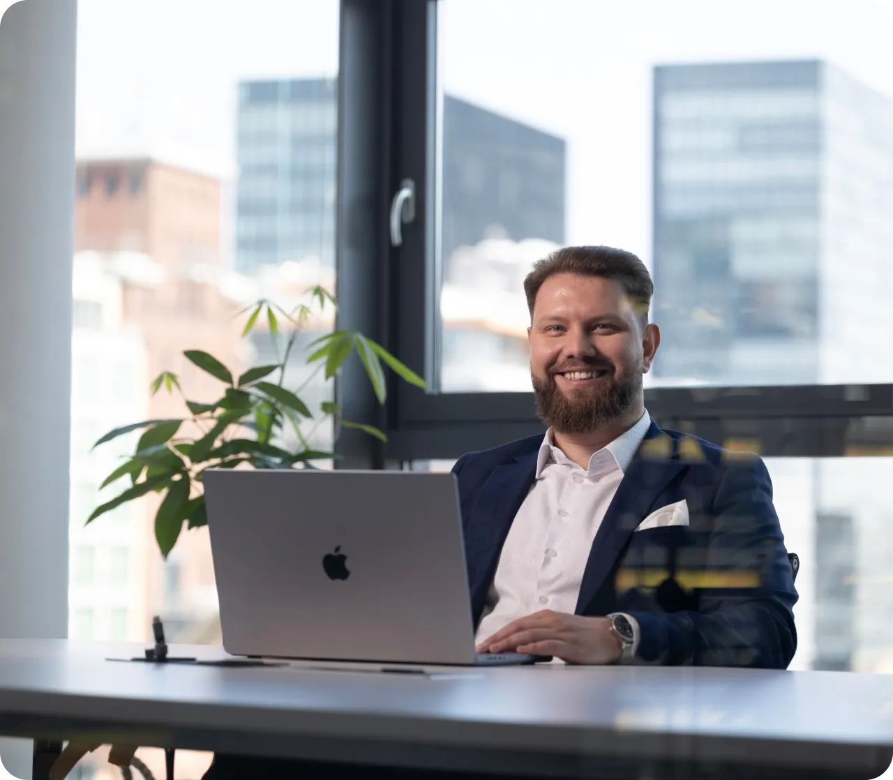 Smiling professional at a desk with a laptop in a modern office - Havedevs, your go-to partner for web app development. Enhance your business operations with innovative web application solutions from Havedevs.